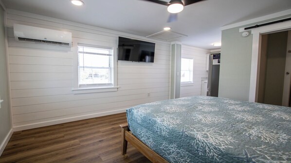 A bedroom with a bed, wooden flooring, white walls, and a ceiling fan.