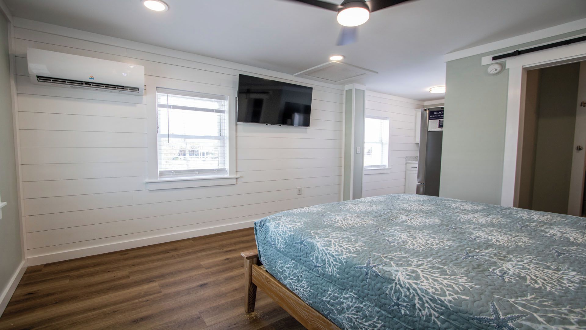 A bedroom with a bed, wooden flooring, white walls, and a ceiling fan.
