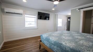 A bedroom with a bed, wooden flooring, white walls, and a ceiling fan.