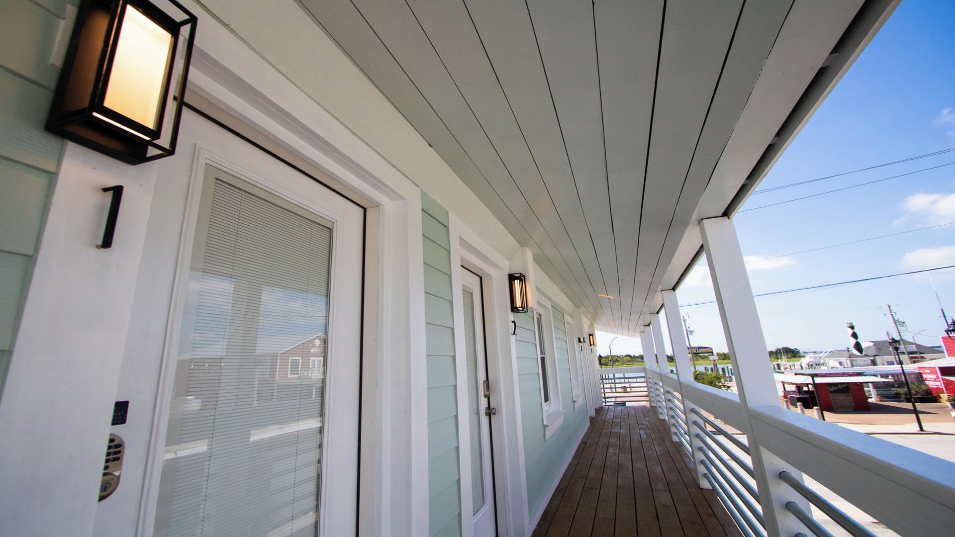 A covered porch with a railing, doors, and exterior lighting fixtures.
