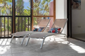 Two lounge chairs with floral cushions, positioned on a tiled floor with a view of greenery through a glass door. - Casa Divers Dream - Screened porch and shared pool! (Kralendijk)