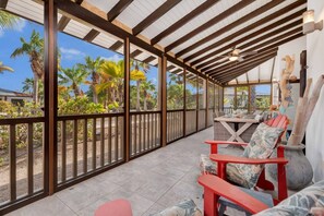 A covered outdoor area with a table and chairs, a ceiling fan, and a view of palm trees. - Casa Divers Dream - Screened porch and shared pool! (Kralendijk)