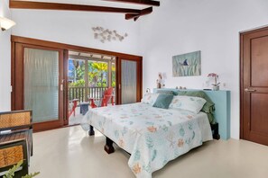 A bedroom with a bed, a nightstand, a chair, a window with a view of palm trees, and a door. - Casa Divers Dream - Screened porch and shared pool! (Kralendijk)
