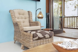 A wicker lounge chair with a cushioned seat and backrest, a patterned pillow, and a small table with a bowl. - Casa Divers Dream - Screened porch and shared pool! (Kralendijk)