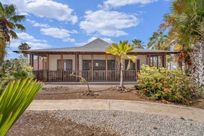 A two-story building with a covered porch, surrounded by palm trees and a gravel driveway. - Casa Divers Dream - Screened porch and shared pool! (Kralendijk)