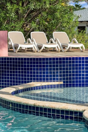 Area piscina con pareti in piastrelle blu e vasca idromassaggio. Sono disposte attorno alla piscina poltrone da relax bianche.