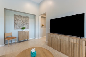 A modern living room with a flat-screen TV, a wooden cabinet, a cushioned chair, and a decorative wall piece.