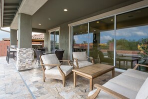 Un patio al aire libre con piso de piedra, una parrilla y una zona de estar con sillas y una mesa.