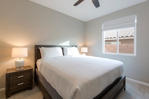 A bedroom with a bed, two bedside lamps, a nightstand, a ceiling fan, and a window with a view of a brick wall.