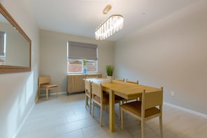 A dining area with a wooden table and chairs, a window with blinds, a potted plant, and a mirror on the wall.