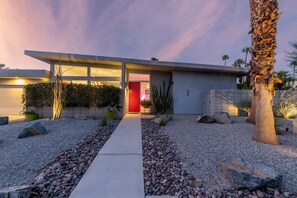 A modern house with a concrete facade, a red door, and a gravel pathway leading to the entrance. - Flamingo Oasis | Private Pool & Spa | Firepit | Sleeps 6 (Palm Springs)