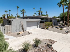 A modern two-story house with a garage, surrounded by palm trees and desert landscaping. - Flamingo Oasis | Private Pool & Spa | Firepit | Sleeps 6 (Palm Springs)