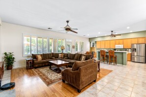 A spacious living room with a large sectional sofa, a coffee table, and a dining area with a kitchen in the background. - Whitehawk Villa | Private Pool & Spa | 3BR | Palm Desert (Palm Desert)