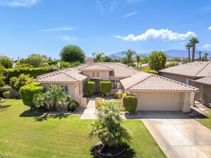 A two-story house with a tiled roof, a front yard with a palm tree, and a mountain range in the background. - Whitehawk Villa | Private Pool & Spa | 3BR | Palm Desert (Palm Desert)