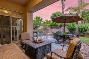 Ein Außenbereich mit Terrasse, einem Feuerbereich, Sitzgelegenheiten und Blick auf Pool und Garten.