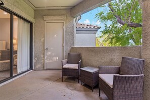 A balcony with wicker furniture, a sliding glass door, and a view of trees and a building. - Horizon Hideaway | Balcony | Pool & Spa | North Scottsdale (Scottsdale)