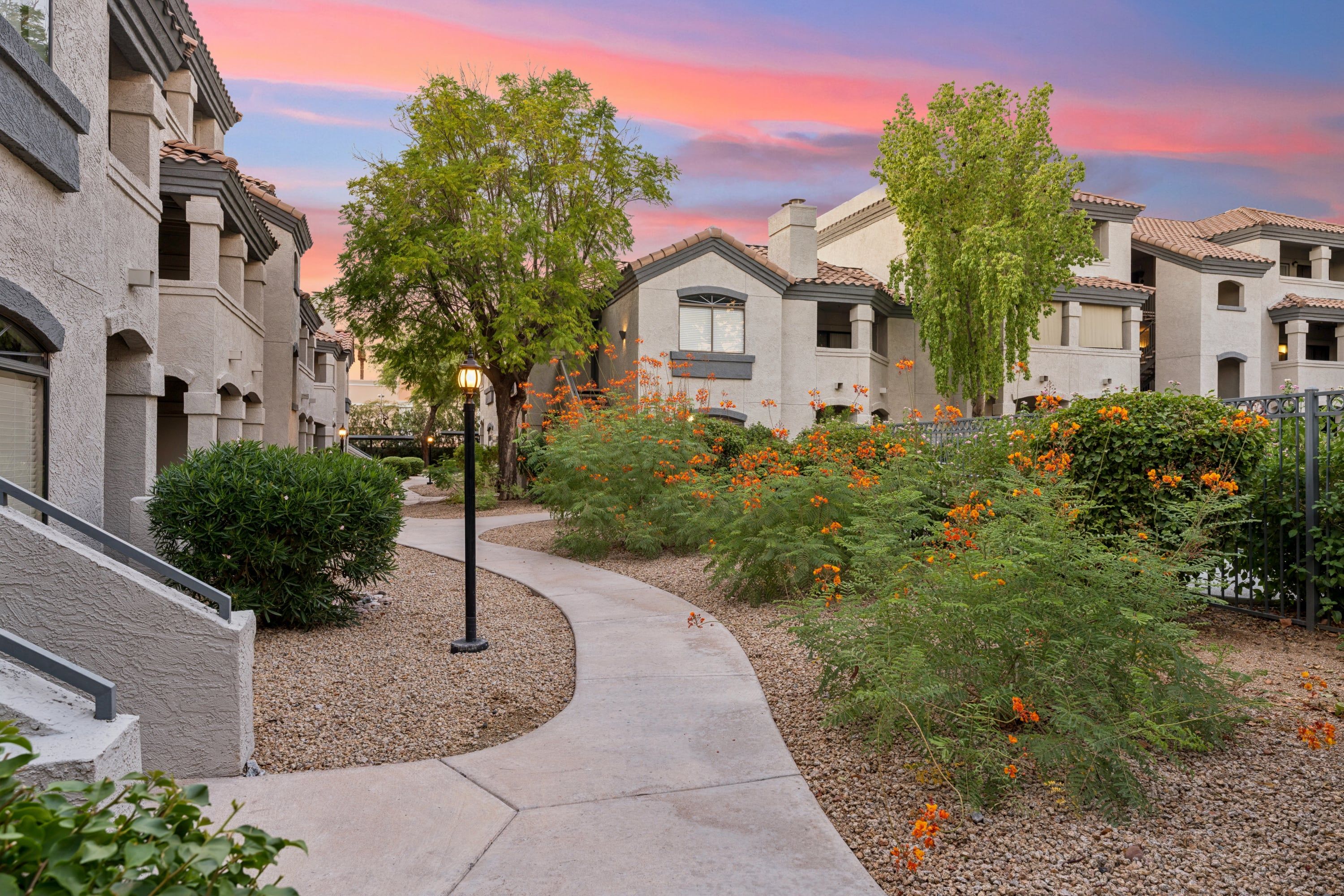 Un quartier résidentiel avec un chemin sinueux, des maisons à l’architecture similaire et une grande variété de plantes, notamment des arbres et des plantes à fleurs.