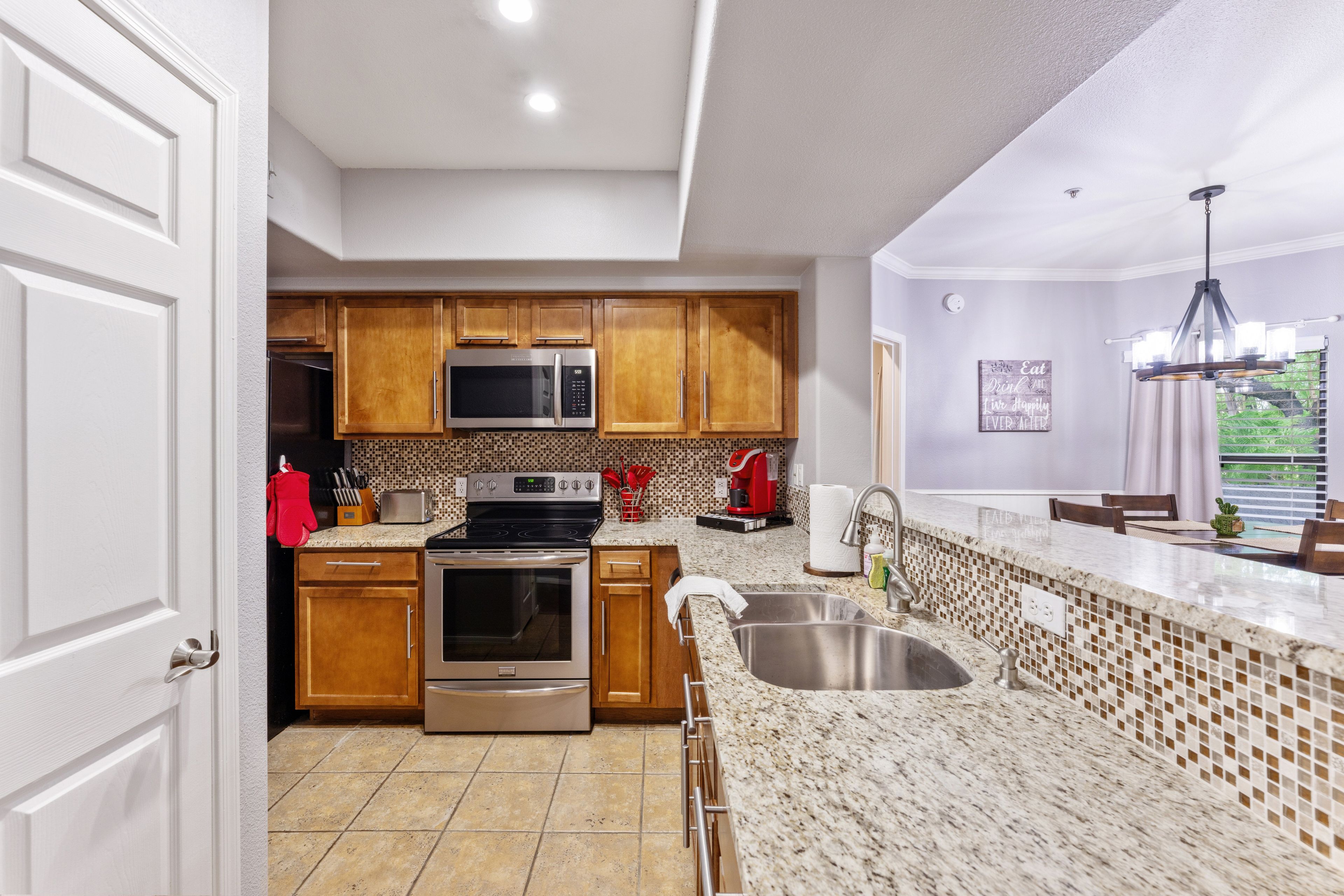 A modern kitchen with wooden cabinets, stainless steel appliances, a tiled backsplash, and a granite countertop.