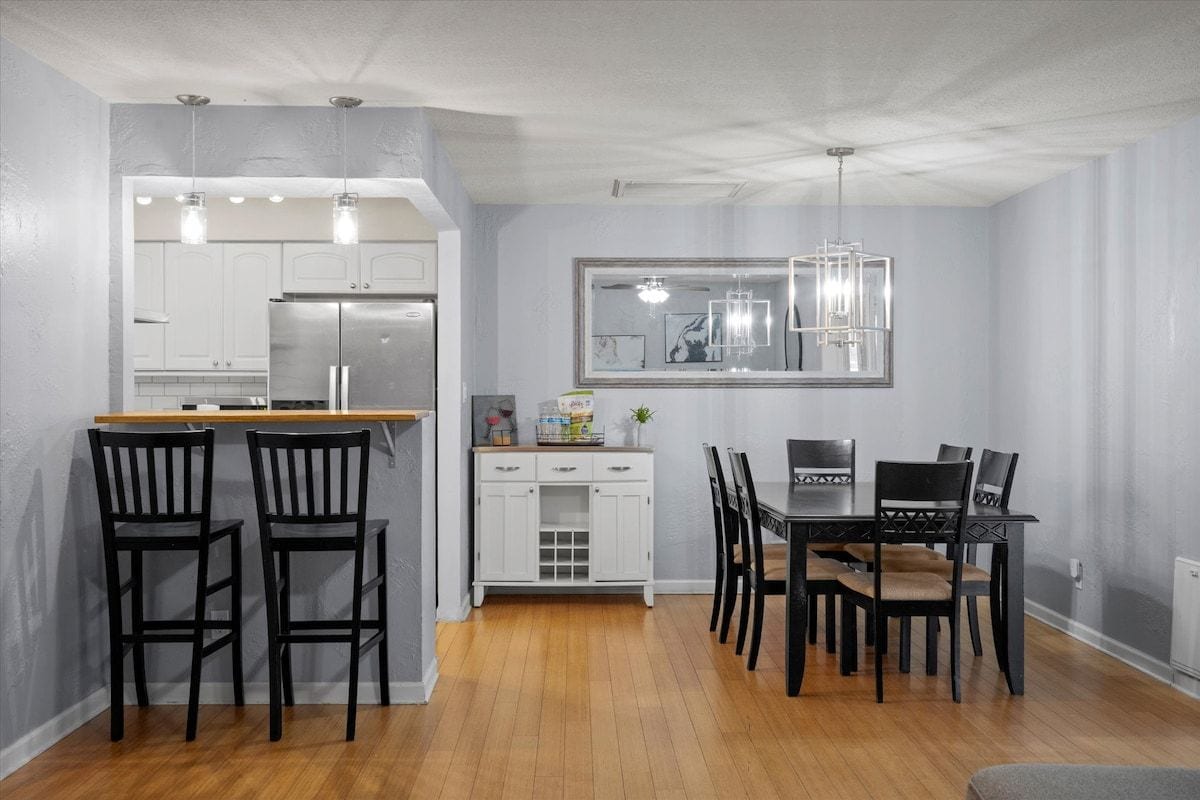 A modern kitchen with white cabinets, a dining area with a wooden table and black chairs, and a pendant light above the table.