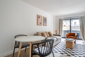 Ett modernt vardagsrum med en soffa, ett runt bord, två stolar, en rutig matta och ett fönster med gardiner.