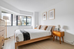 Ein modernes Schlafzimmer mit einem Holzbett, Nachttischen und einem Fenster mit Jalousien.