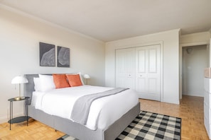 A bedroom with a bed, bedside lamps, a checkered rug, and a door to a hallway. - Blueground | Fenway–Kenmore, gym, nr Fenway Park (Boston)