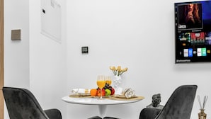 Ein moderner Essbereich mit einem runden Tisch für zwei Personen, komplett mit einer Obstplatte, einem Glas Orangensaft und einer Vase mit Blumen.