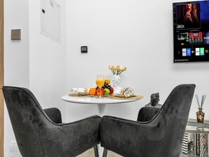 Moderni ruokailutila, jossa on pyöreä pöytä kahdelle, ja pöydällä on hedelmävati, lasi appelsiinimehua sekä maljakko kukkineen.