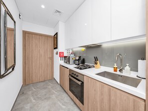 A modern kitchen with a stove, sink, and wooden cabinets. - Stylish Luxury Canal View Studio, Business Bay (Dubai)