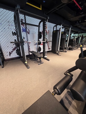 A gym with various exercise equipment, including a squat rack, benches, and weight machines. - Stylish Luxury Canal View Studio, Business Bay (Dubai)