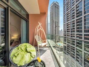 A balcony with a hanging chair, a green cushion, and a glass table with two glasses of orange juice. - Stylish Luxury Canal View Studio, Business Bay (Dubai)