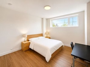 Ein Schlafzimmer mit einem Bett, Nachttischlampen, einem Holznachttisch, einem schwarzen Tisch und einem Fenster mit Blick.
