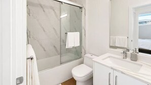 Ett modernt badrum med en dusch som är avskärmad med glasväggar, en vit toalett och ett handfat med en spegel.