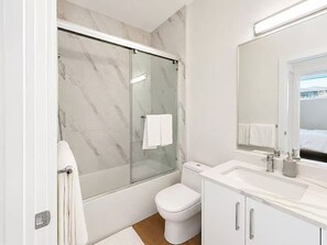 Ein modernes Badezimmer mit einer Duschkabine, einer weißen Toilette und einem Waschtisch mit Spiegel.