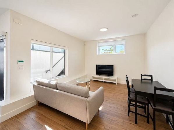 Un salon moderne comprenant un canapé, un téléviseur, une table à manger avec des chaises et un escalier menant à un niveau supérieur.