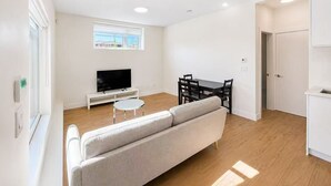 Ett modernt vardagsrum med en soffa, en tv, ett matbord med stolar och ett fönster med utsikt.