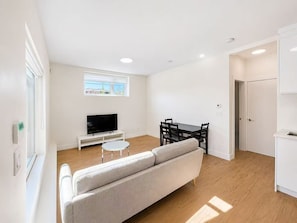 Ein modernes Wohnzimmer mit einer Couch, einem Fernseher, einem Esstisch mit Stühlen und einem Fenster mit Blick.