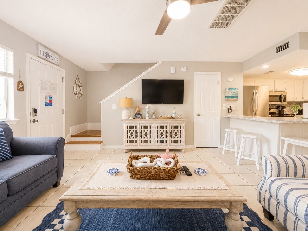 A living room with a sofa, a coffee table with a basket, a TV, and a kitchen area with stools.
