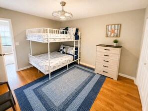 A bunk bed with a storage chest beside it, a blue patterned rug, and a ceiling light fixture. - Golf Cart | 4BR | Sleeps 9 | Mini Golf | Pool (Panama City Beach)