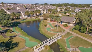 A residential area with a golf course, a small bridge, and houses with sloped roofs. - Golf Cart | 4BR | Sleeps 9 | Mini Golf | Pool (Panama City Beach)
