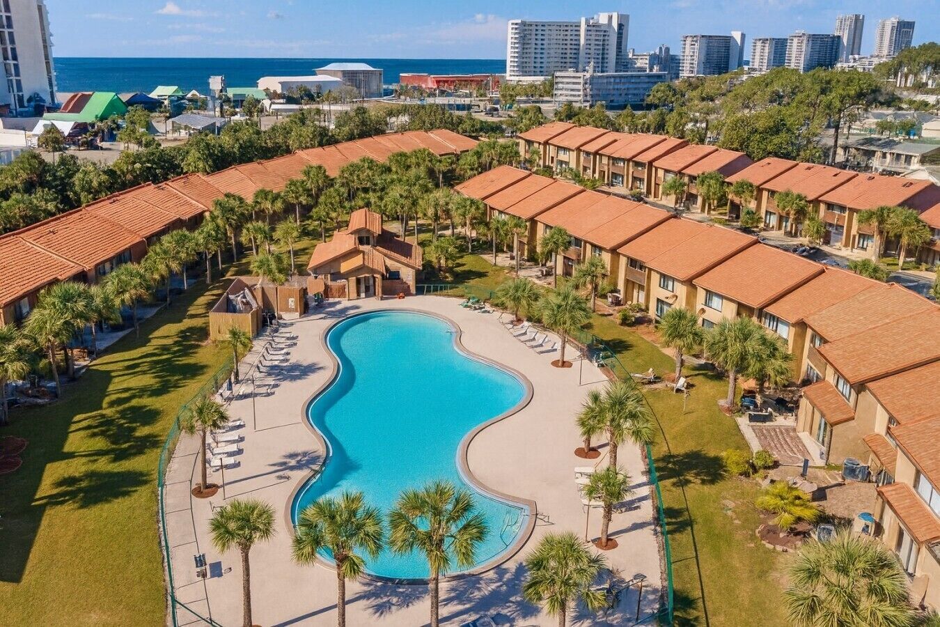 Un resort con una amplia piscina, varias cabañas tipo bungalow y vista al océano.