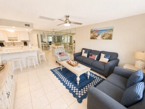 A spacious living area with a sofa, coffee table, and a dining area with chairs. - Golf Cart | 4BR | Sleeps 9 | Mini Golf | Pool (Panama City Beach)