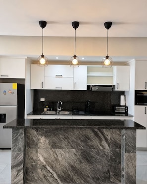 A modern kitchen with a marble island, black countertops, white cabinets, and pendant lighting. - 2BR 10 Min Walk to Beach Private Rooftop BBQ (Punta Cana)