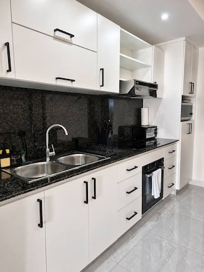 Cozinha moderna com armários brancos, bancadas pretas e eletrodomésticos de aço inoxidável.