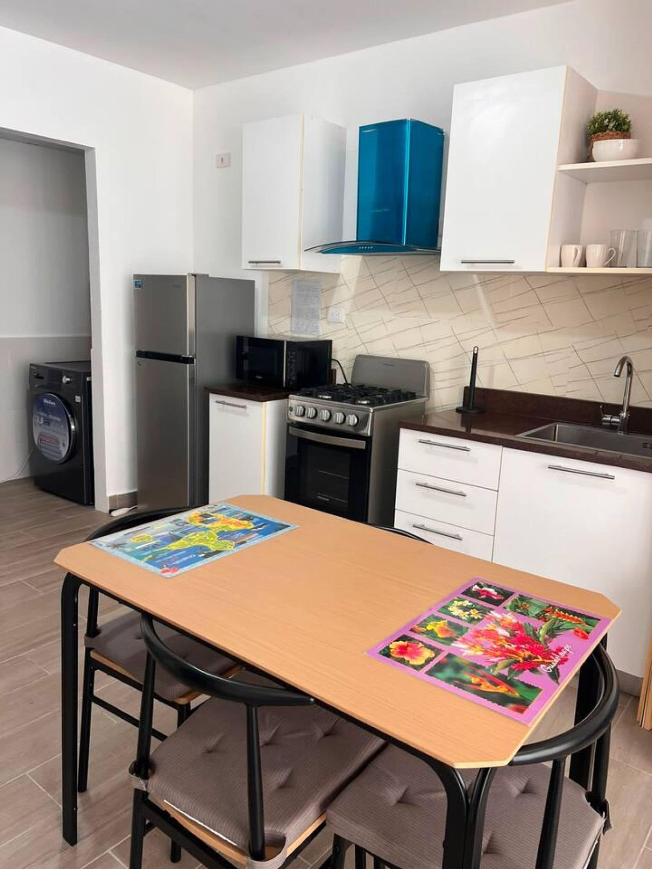 Una cocina moderna con armarios blancos, una campana extractora azul, un refrigerador de acero inoxidable, un microondas, una estufa a gas y un lavavajillas.