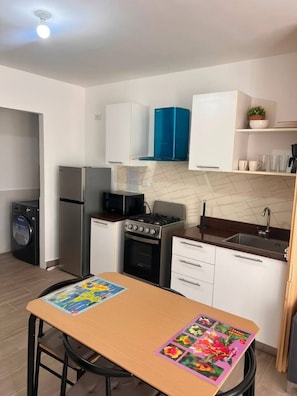 A compact kitchen with a washing machine, a refrigerator, a stove, and a sink. - Charming 1BR Pool Gym Electricity Included (Punta Cana)
