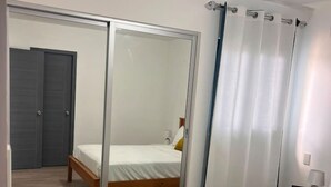 A hotel room with a bed, a mirror, a wardrobe, and a curtain. - Relaxing 1BR Stay Gated Community (Punta Cana)