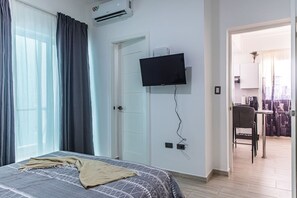 Ein Hotelzimmer mit einem Bett, einem an der Wand befestigten Fernseher, einer Tür und Blick auf die Stadt durch das Fenster.