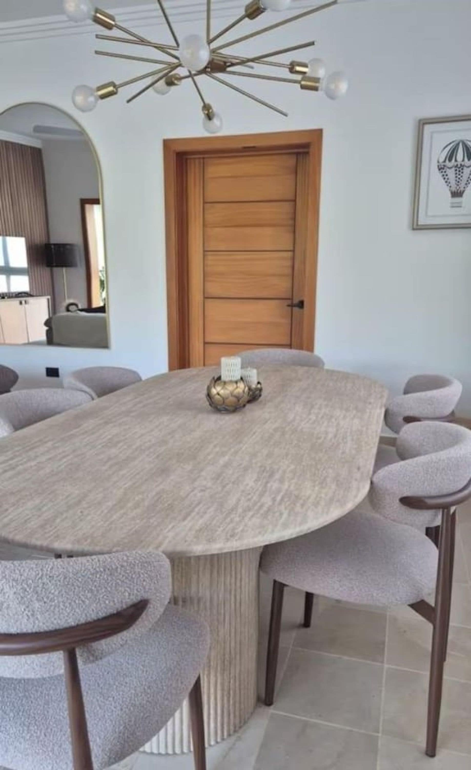 Uma área de jantar moderna com mesa redonda, cadeiras estofadas cinzentas, um objeto decorativo central e uma luminária contemporânea.