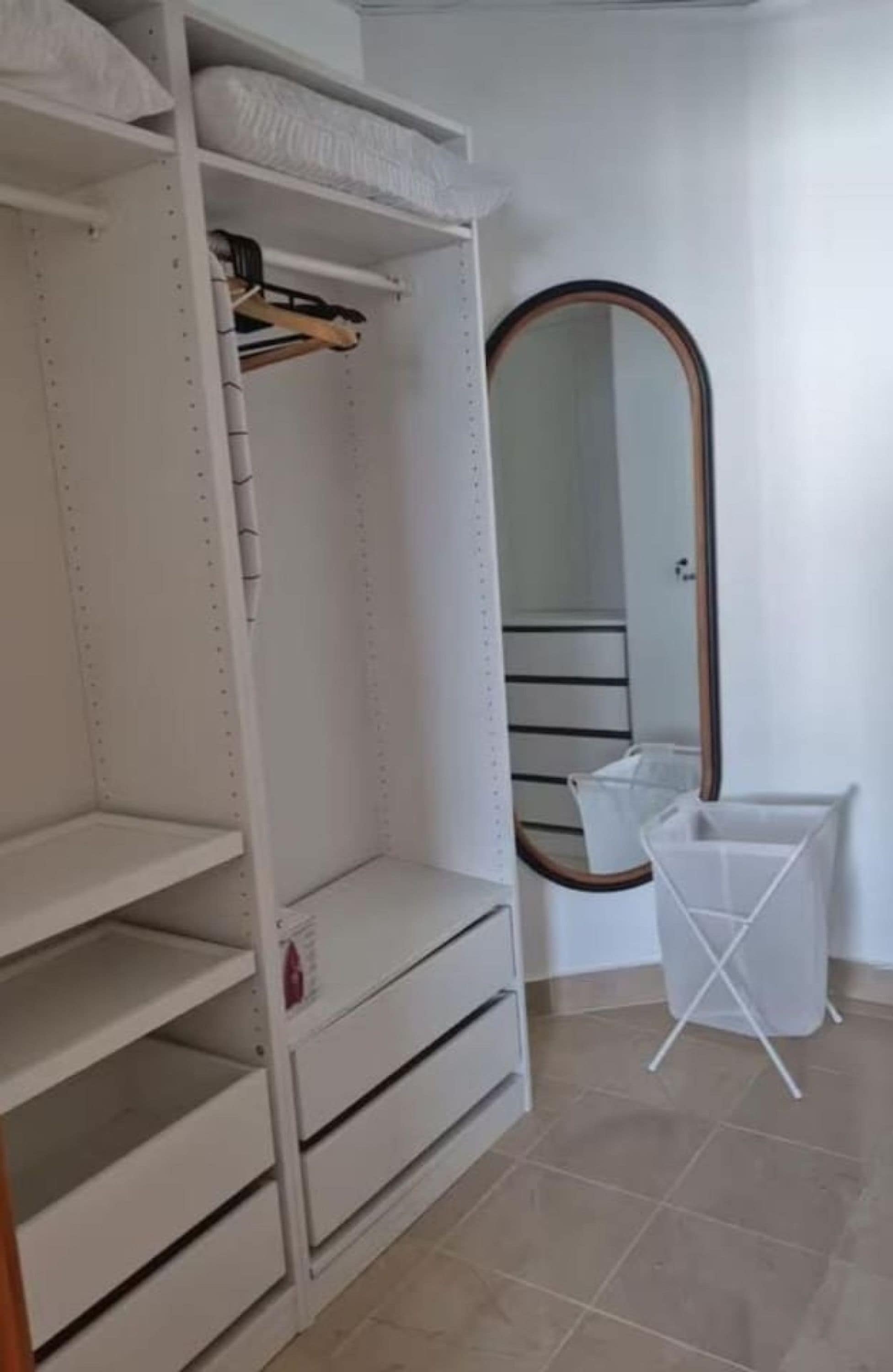 A closet with shelves and hanging space, a mirror, and a laundry basket.
